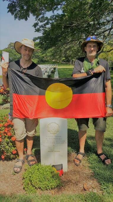 Mark Powell and John Parkinson unfurl an Aboriginal flag next to the grave of Harry Saunders, of Condah, who died on the Kokoda Trail.