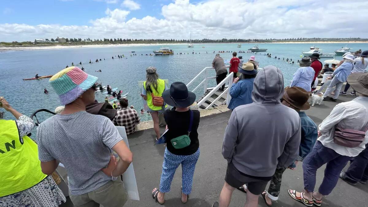 A large crowd gathers at the breakwater in Warrnambool to watch protesters gather into a circle on the water.