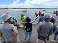 A large crowd gathers at the breakwater in Warrnambool to watch protesters gather into a circle on the water.