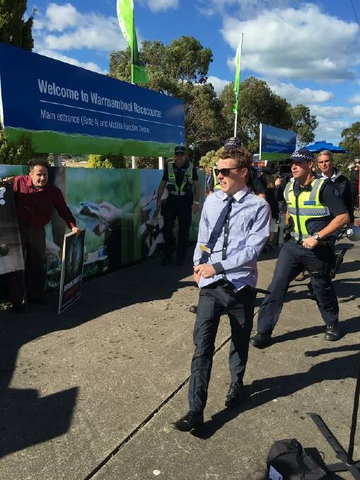 A 22-year-old Warrnambool man is escorted from the track by police after pouring a beer over a protester.