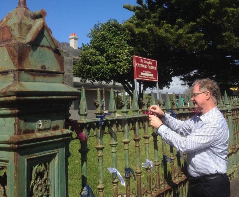 Healing: St Joseph's Catholic Church's Father John Fitzgerald ties a ribbon to the church's fence as part of the Loud Fence campaign that aims to support sexual abuse victims, survivors and their families. Picture: Peter Blenkiron