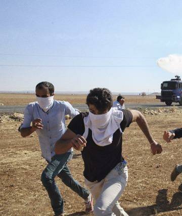 Kurdish protesters on the border near the besieged Syrian town of Kobane flee tear gas fired from a Turkish riot control vehicle on Tuesday. Photo: Andrew Quilty/Oculi