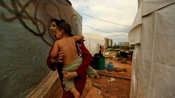 A Syrian refugee from Homs carries her child past makeshift homes in the unofficial refugee camp on the outskirts of Barsa, near Tripoli. Photo: Kate Geraghty