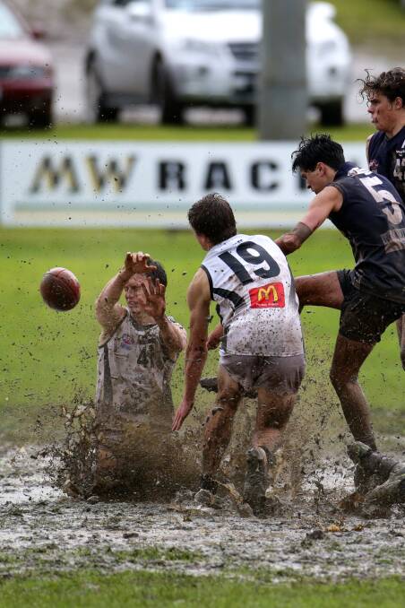 North Ballarat Rebels Liam Howarth (left) and Tom Schnerring cop the mud spray as Geelong Falcon Aaron Christensen blasts a kick in heavy conditions at Reid Oval.