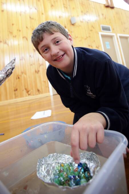 Warrnambool West Primary School pupil Rhys Bellman, 12, adds marbles to a foil boat to test its capacity before it sinks. 140724DW01 Picture: DAMIAN WHITE