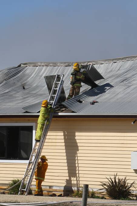 Firefighters lift roofing iron from the still-burning house on Wangoom Road. 