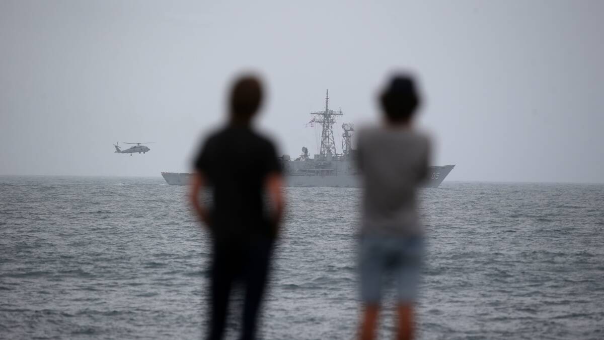 People gathered to watch the HMAS Melbourne at Lady Bay, while a Seahawk helicopter hovered around and let off a flare.