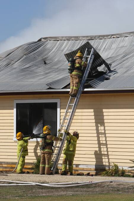 Firefighters lift roofing iron from the still-burning house on Wangoom Road. 