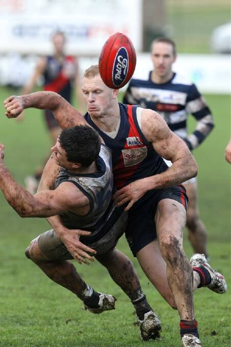 Geelong’s Dominic Gleeson gets a desperate handpass clear as he is upended by Coburg’s Kelvin Moore in yesterday’s muddy scrap at Warrnambool’s Reid Oval. 