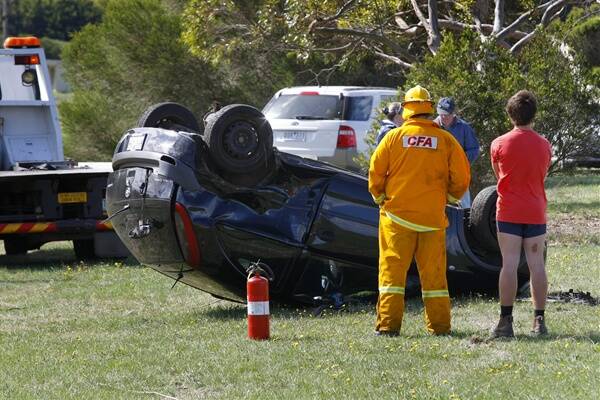 A bystander and Purnim CFA members look at a Barina that overturned on the Hopkins Highway on Easter Saturday.