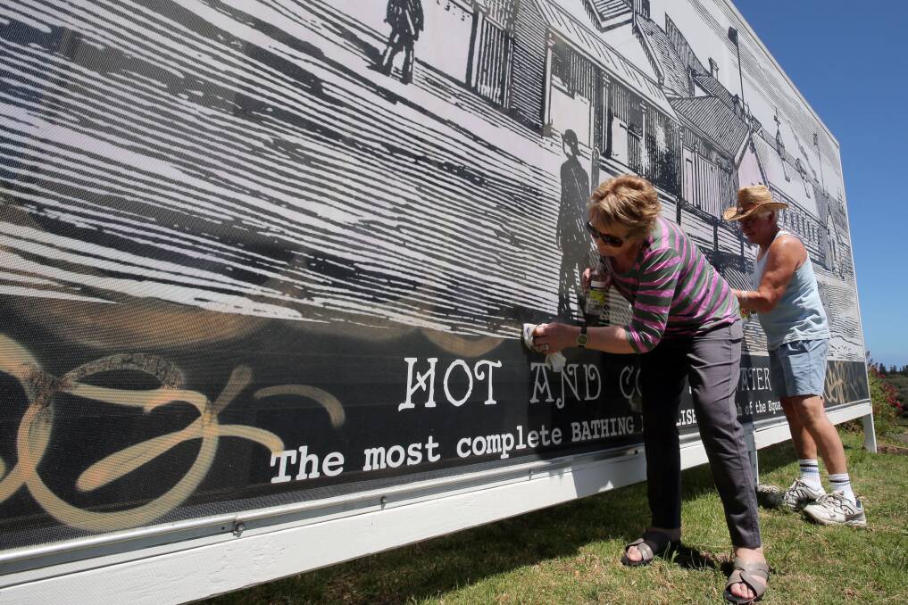 Warrnambool and District Historical Society president Glenys Phillpot and committee member Andrew Suggett use citrus solvent to remove graffiti from a mural at History House.  