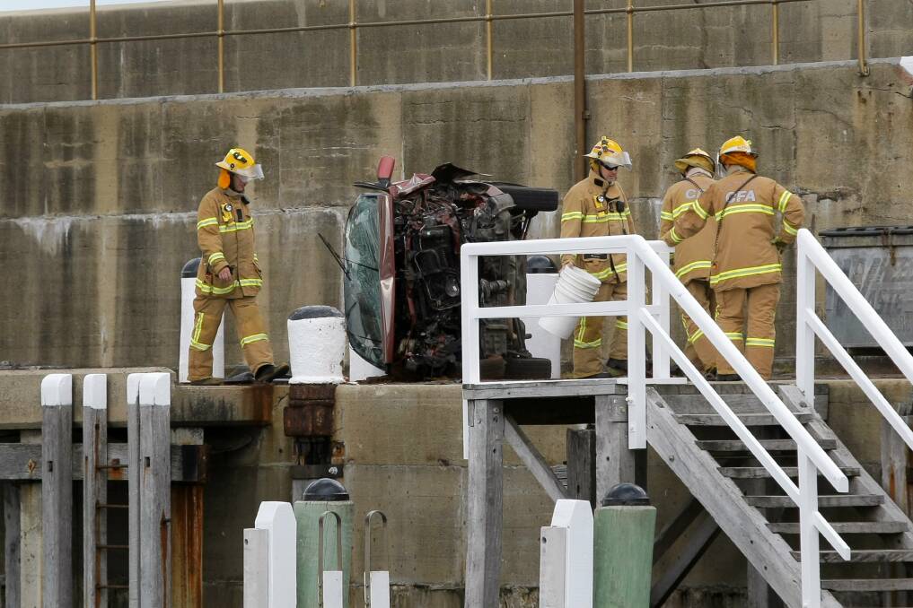 CFA officers clean up around a badly-damaged car which crashed into bollards on the Warrnambool breakwater yesterday. 