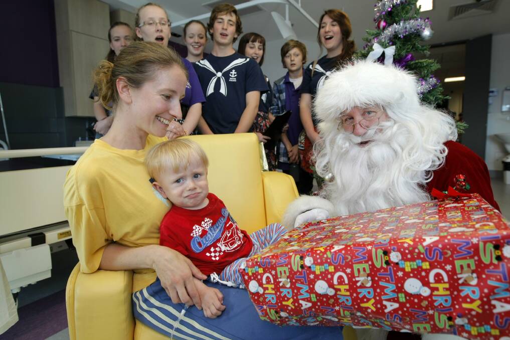 Anna Reilly does her best to reassure her son William, 19 months, as Santa hands over a gift during a Christmas visit to the paediatric ward at South West Healthcare. 