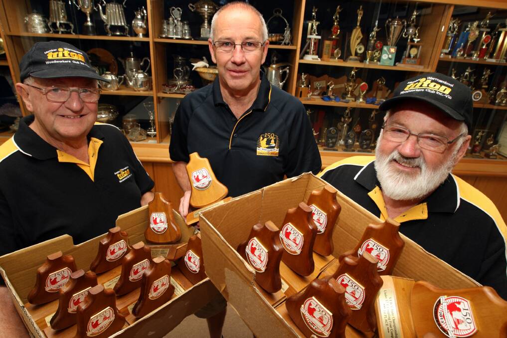 Warrnambool Triton Woodworkers members Stewart Trigg (left) and David Carter display the handcrafted bell-shaped trophies for  the coming state urban brigade championships to Warrnambool Fire Brigade chairman Malcolm Bishop. 