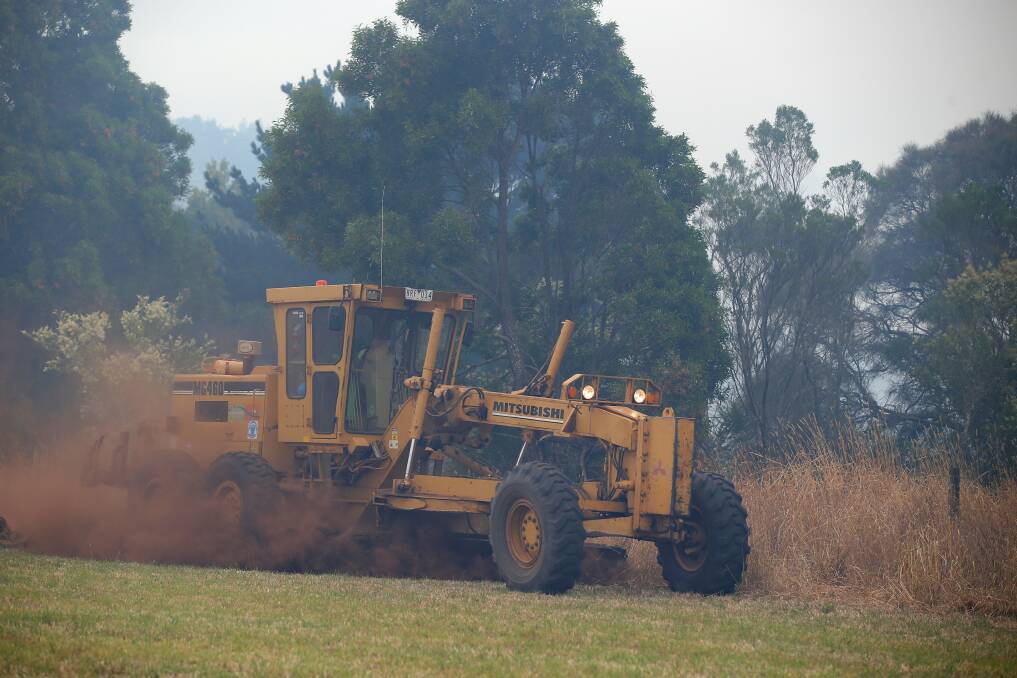 A grader makes a containment line to stop embers from reaching farm land.