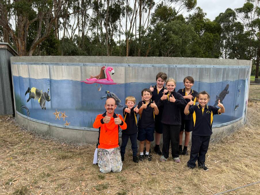 Warrnambool artist Jimmi Buscombe kneels with children from Merino Consolidated School in front of the new mural. 
