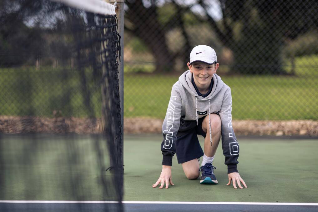 Warrnambool's Luke Robson, 13, kneeling next to a tennis net as he celebrates being selected as an Australian Open 2024 ball kid. Picture by Sean McKenna