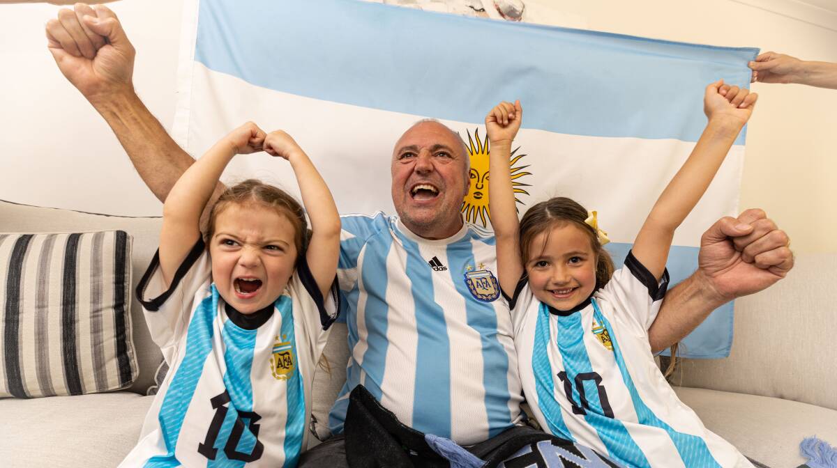 Sandro Schietroma, middle, leads an Argentinian cheer for the FIFA World Cup final with granddaughters Bailey Zeunert, left, and Isla Zeunert, right. Picture by Sean McKenna