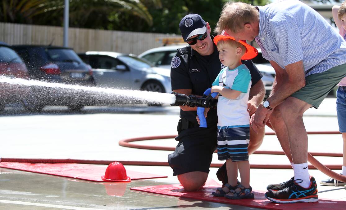 READY, AIM: Lachlan Kerr, 2, practises his aim with the water hose with the help of his pa Bruce and firefighter Scott Lilley. 