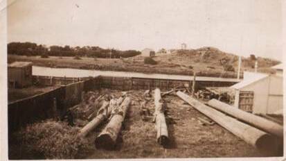 EARLY CONSTRUCTION: Logs being squared with 1944 battery hill in the background.