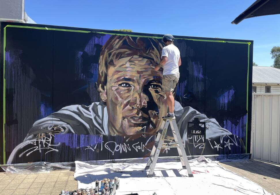Melbourne artist Ling works on his mural of Shane Warne which adorns the wall of a cafe at Violet Town. Picture supplied.