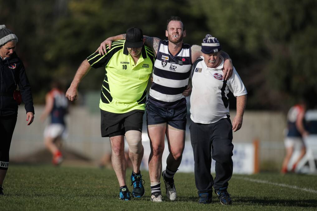 OUCH: Allansford player Brad Williams comes from the field in the hands of the trainers. Picture: Amy Paton