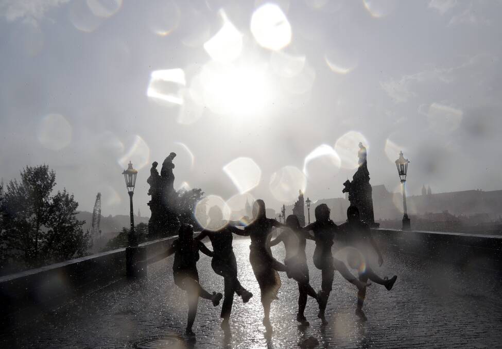 Young girls dance at the medieval Charles Bridge as a heavy rain storm hits Prague, Czech Republic.