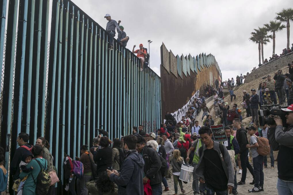 Stand-off: Hundreds of migrants from Central America gather with supporters at the border wall with the US, where it ends at the Pacific Ocean, in Tijuana, Mexico. President Trump is demanding Congress approve funding for a new wall right along the border. Picture: Meghan Dhaliwal