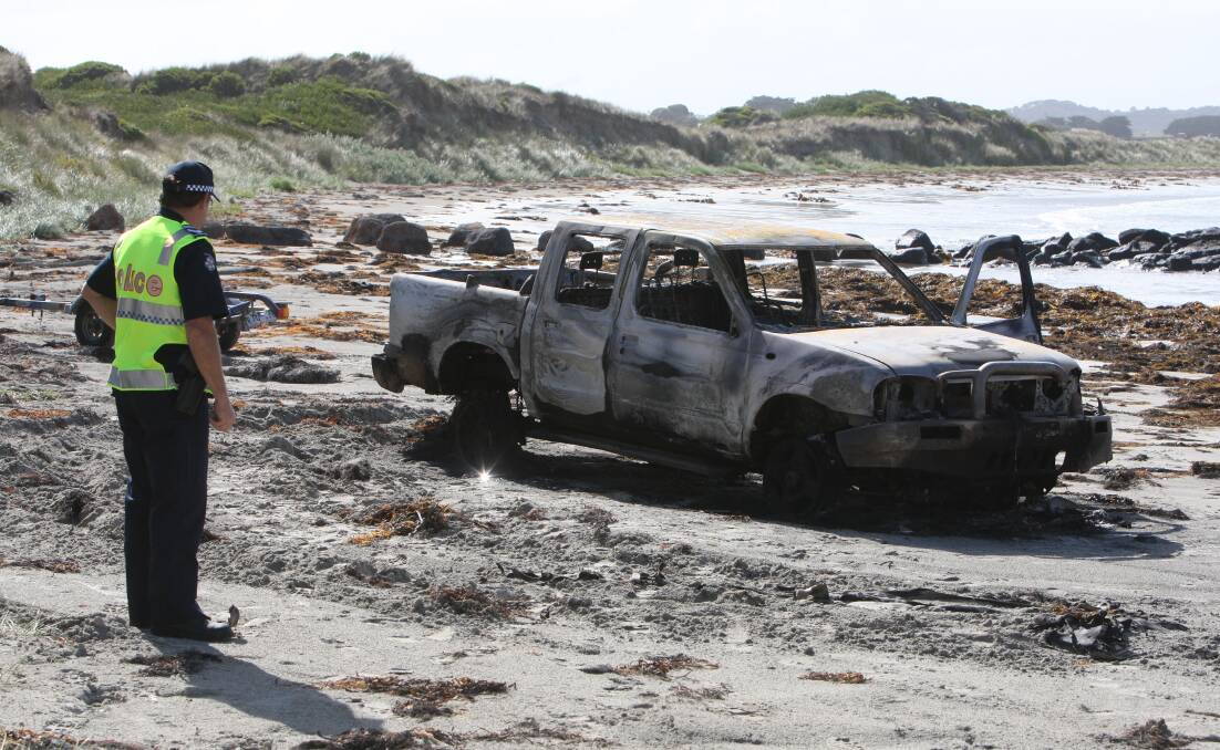 A policeman inspects the burnt-out ute at Killarney beach.