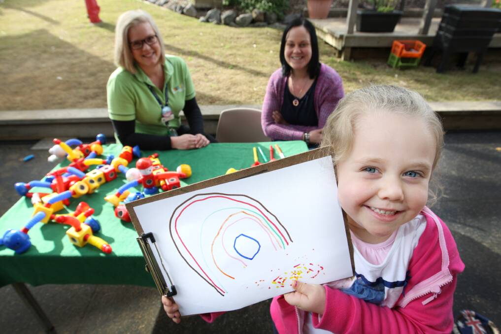 Molly Sheen, 3, shows off her rainbow drawing, watched by her mum Patreena Kelly (back, right) and teacher Sarah McPhail, at City Kinder.
140714AM20  Picture: ANGELA MILNE