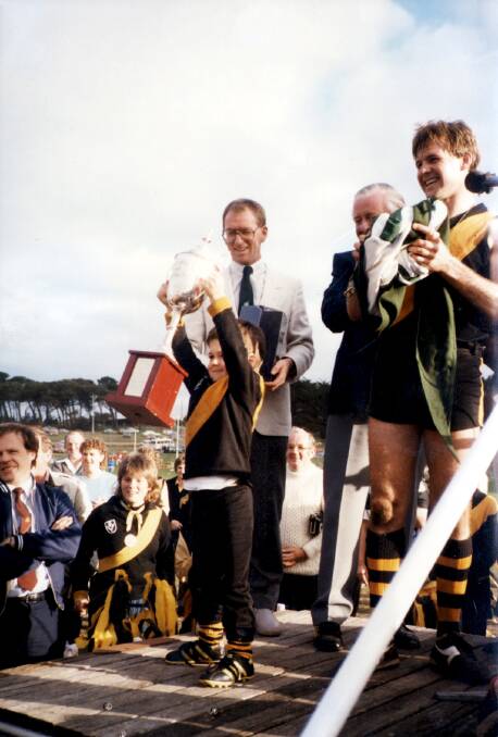 Four-year-old Brown proudly hoists the 1985 Hampden League premiership cup won by Colac, captained by his dad Brian.