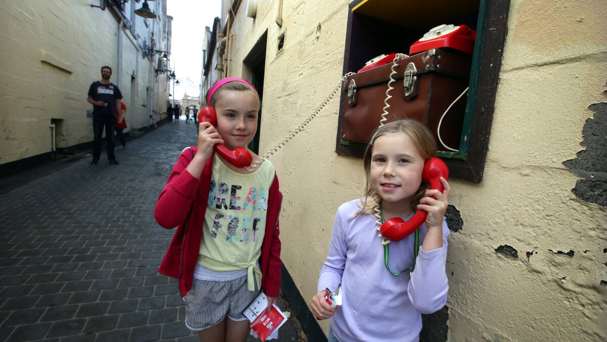 Mia King, 8, and her sister Freya, 6, from Warrnambool getting clues from a telephone in Liebig Lane. 