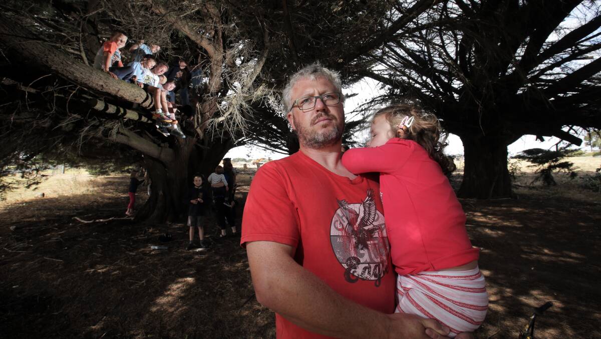 North Warrnambool resident Dean Fleming, holding daughter Sage, 4, along with lots of neighbourhood children, is upset that the cypress trees along Mortlake Road are to be removed. Picture: ROB GUNSTONE