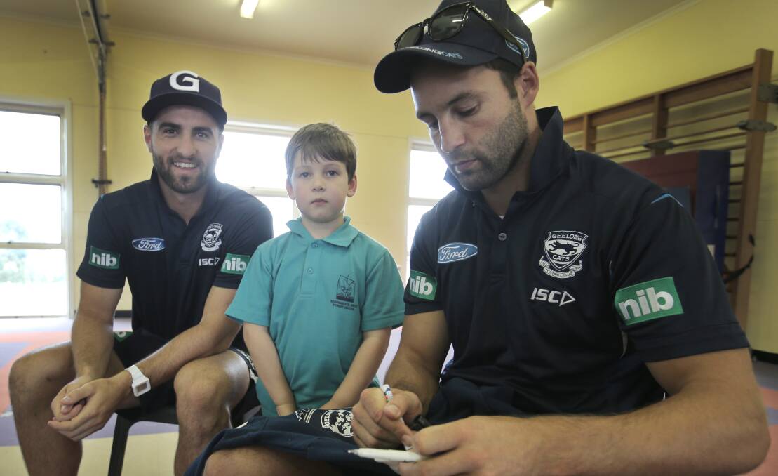 Shane Kersten, Warrnambool West Primary student Oscar Mahony, 6, and player Jimmy Bartel signing an autograph.