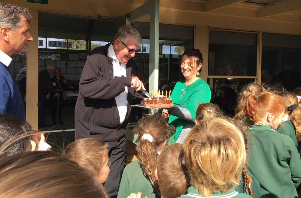 HAPPY: Father Bill van de Camp cuts his birthday cake at St Patrick's Primary School Koroit. Holding the cake is teacher Leisa McCosh.