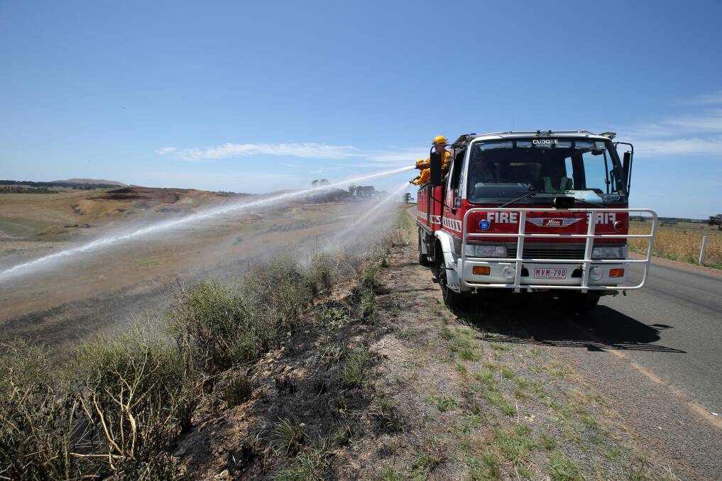 Firefighters spray a blaze beside the Hopkins Falls Road at Cudgee yesterday.  