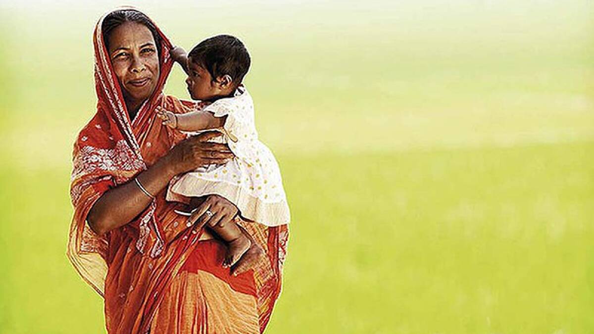 A portrait of Kabita Begum, with her one-year-old daughter, in front of a huge rice paddy. Photo: Andrew Goodwin