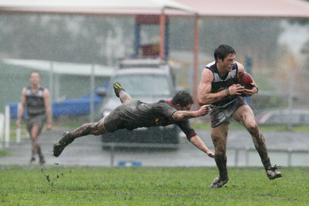 Timboon Demons player Simon Harkness reaches for Allansford's Matthew Dwyer in a wet match. Picture: LEANNE PICKETT